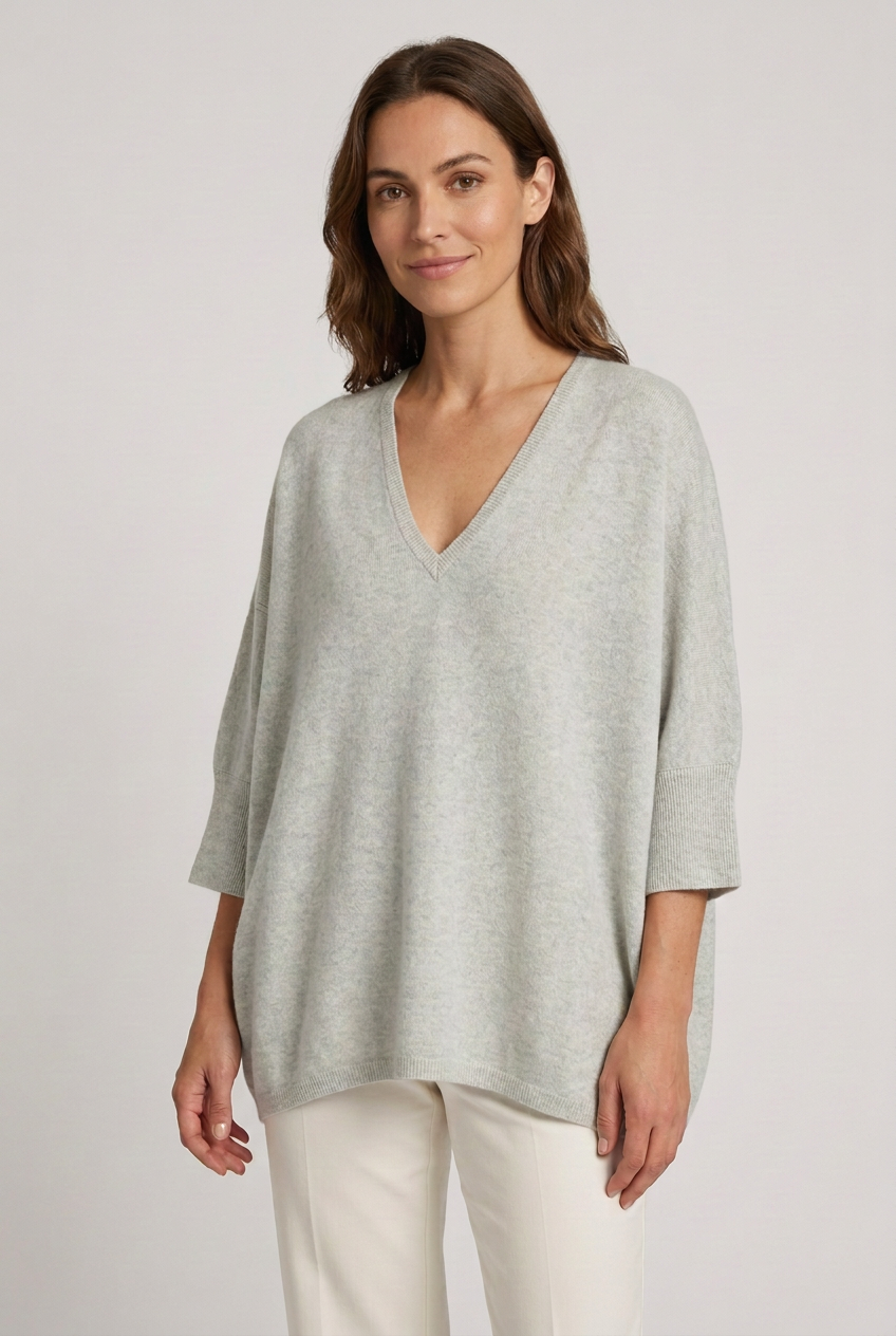 Capa oversized cinzenta-clara de decote em V vestida por modelo com sorriso discreto