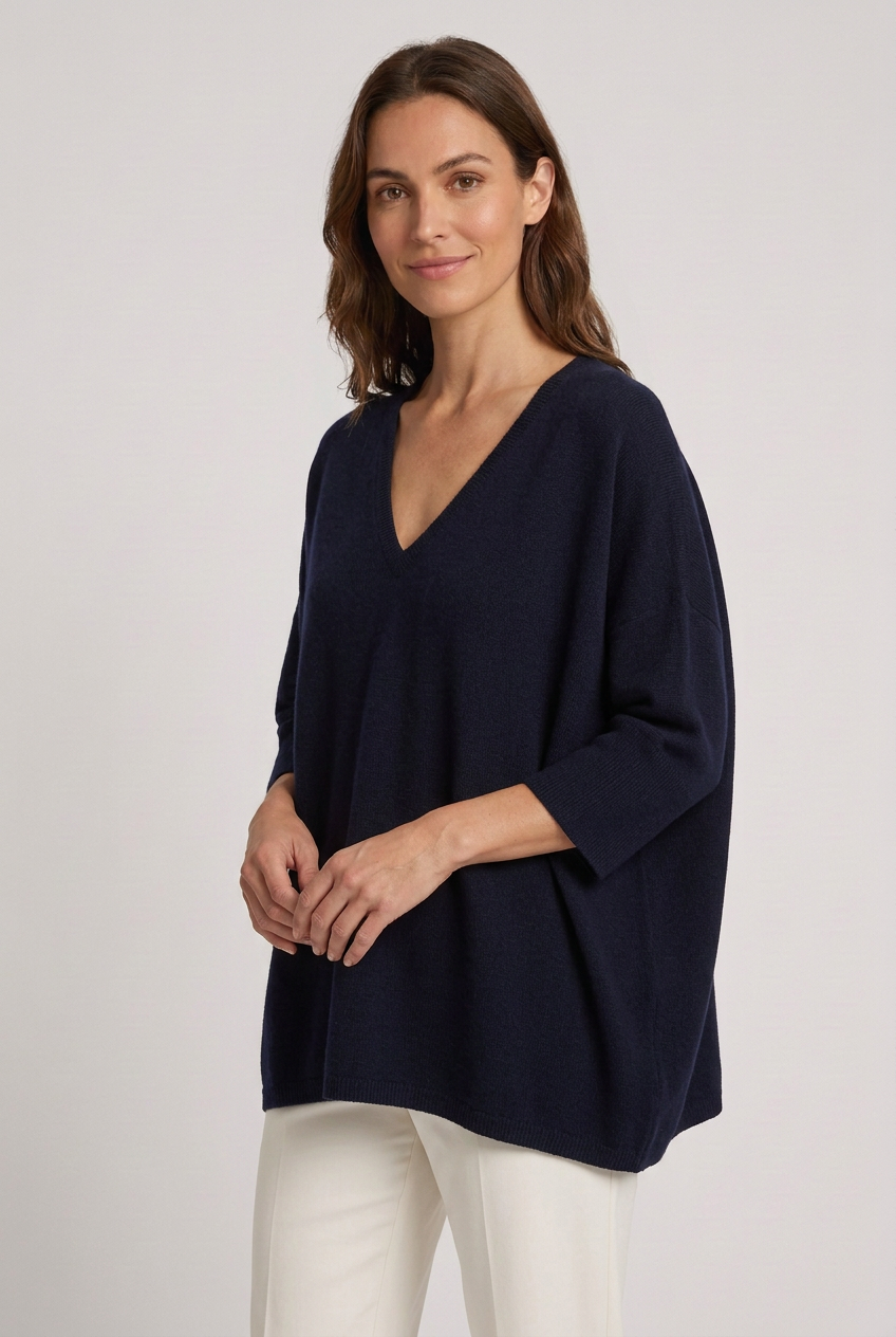 Capa oversized azul-escura com decote em V vestida por modelo com sorriso discreto em pose de três quartos